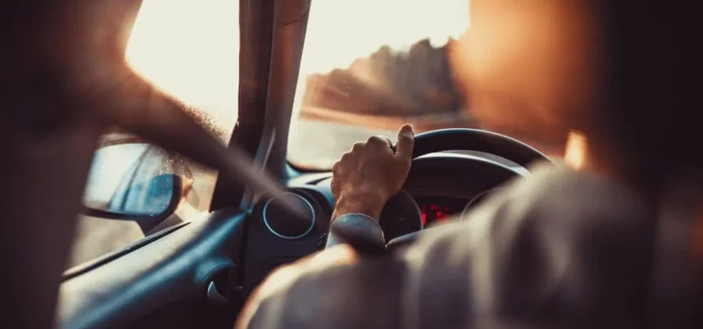 Pessoa dirigindo carro durante trajeto ao pôr do sol representando direção de carro segura