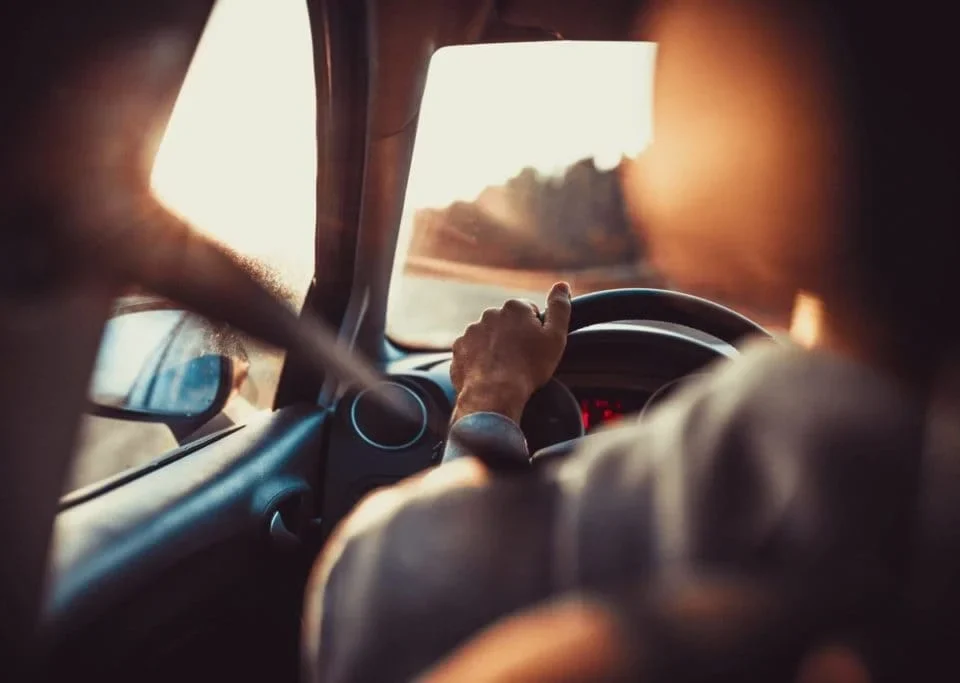 Pessoa dirigindo carro durante trajeto ao pôr do sol representando direção de carro segura
