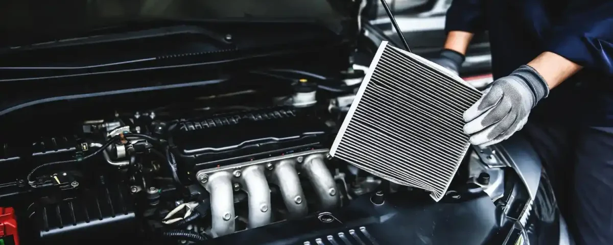 Mecânico realizando manutenção no motor e trocando o filtro de ar próximo ao radiador do carro aberto
