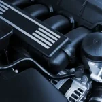 Detalhe de um motor aspirado com componentes visíveis sob o capô de um carro