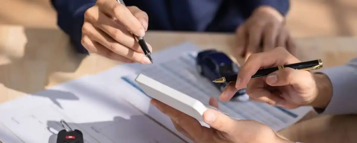 Pessoa assinando contrato de leasing de carros com chave e miniatura de veículo sobre a mesa