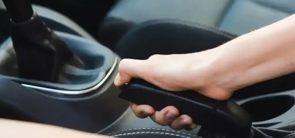 Mão acionando freio de mão em carro, destacando o uso do equipamento de segurança veicular.