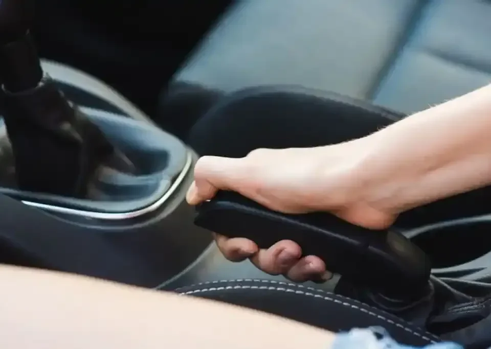 Mão acionando freio de mão em carro, destacando o uso do equipamento de segurança veicular.