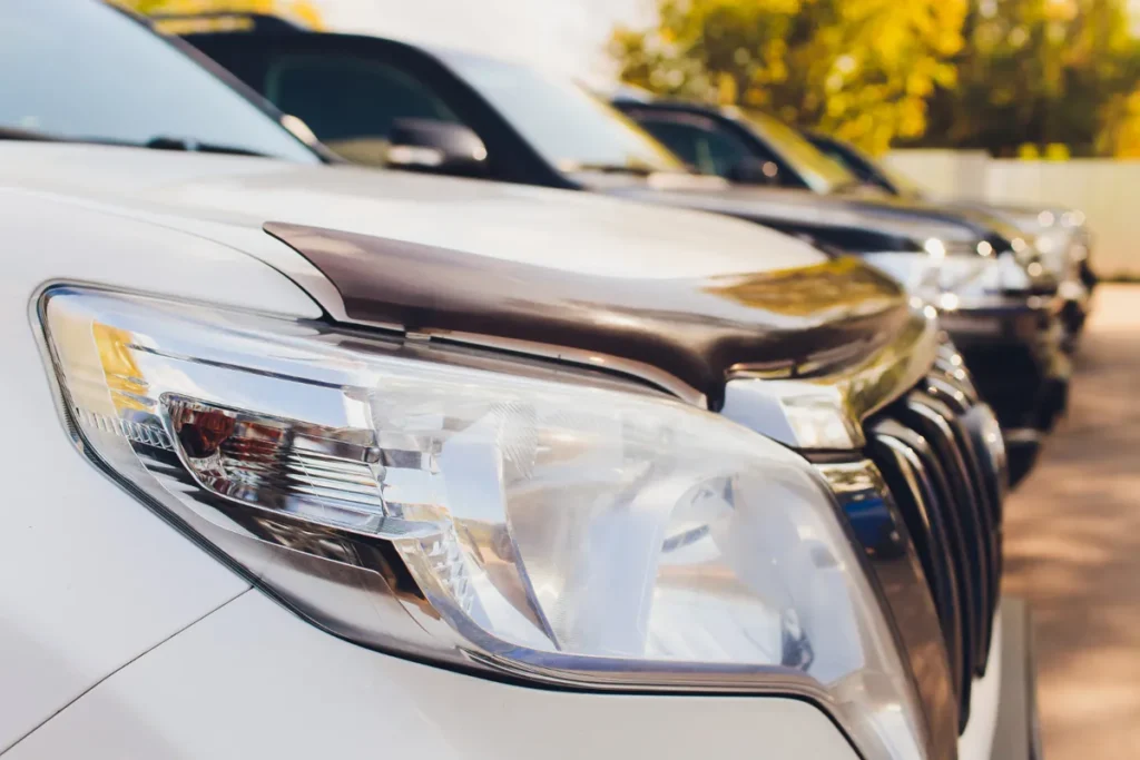 Tipos de farol de carro Farol dianteiro de SUV branco em primeiro plano com fileira de carros ao fundo